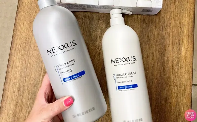A-Hand-Holding-Nexxus-Shampoo-and-Nexxus-Conditioner-on-a-Table.webp